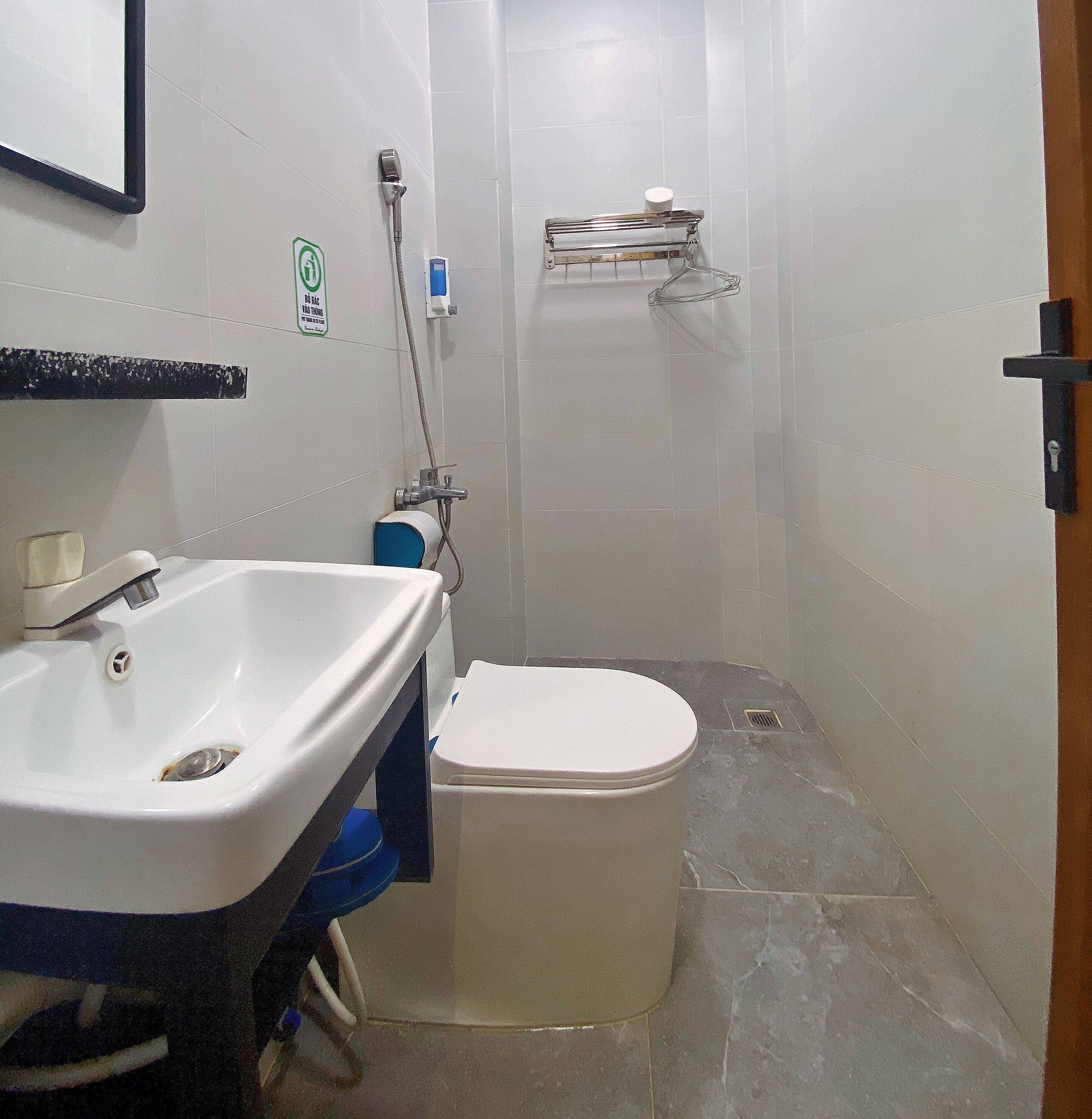 A bathroom with a white sink, toilet, and shower. There is a towel rack and a soap dispenser on the wall.