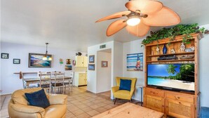 Ein Wohnzimmer mit Fernseher, Deckenventilator, Essbereich und Küche.