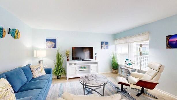 A living room with a blue sofa, a white TV stand, a marble coffee table, and a white armchair.