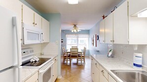 A kitchen with white cabinets, a microwave, an oven, a sink, and a dining area with a table and chairs.