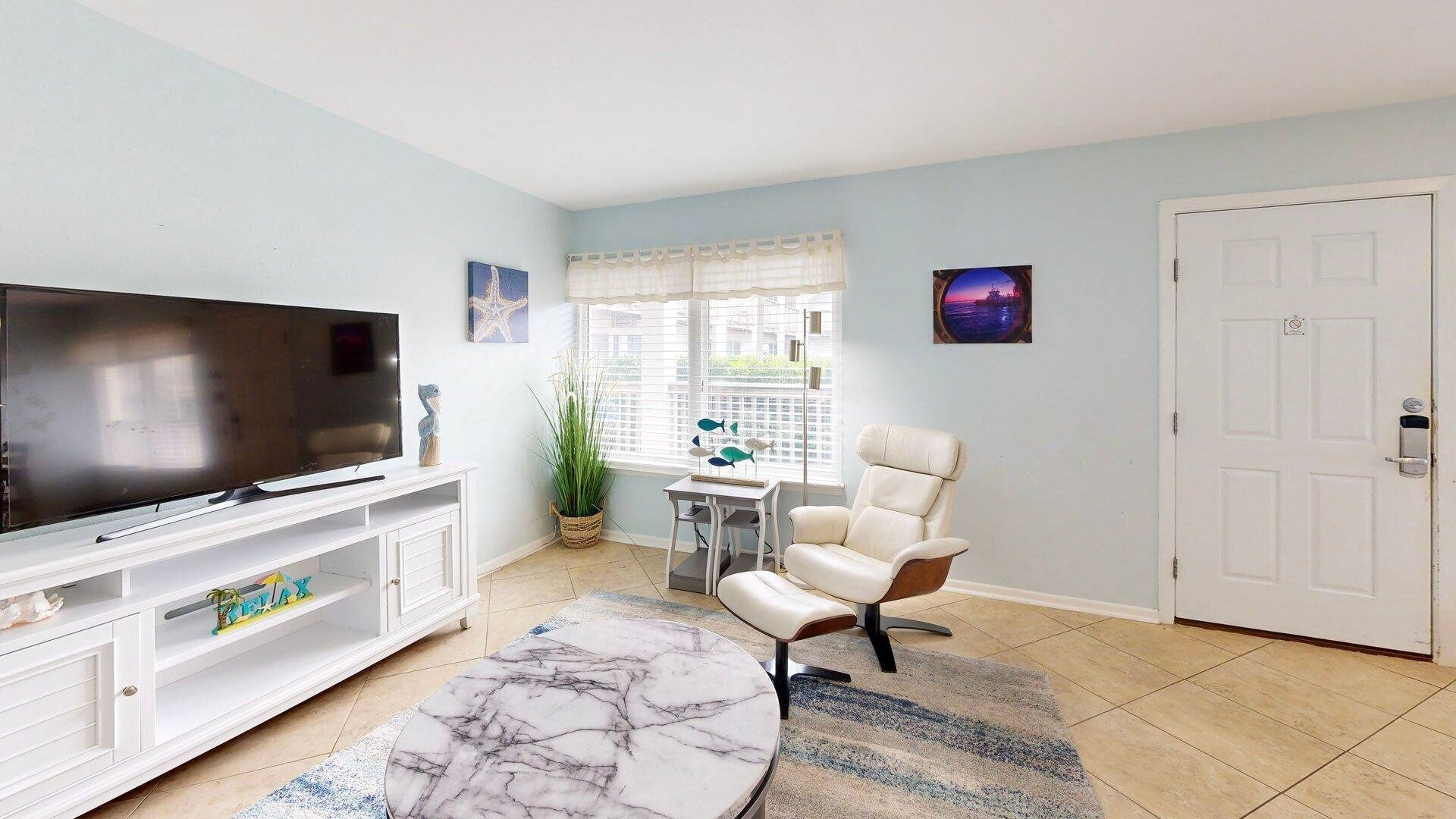 Un salon avec un téléviseur, un canapé blanc, une table basse en marbre et une porte.