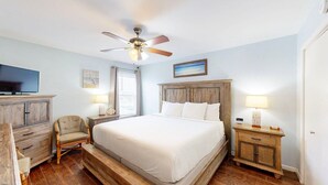 A bedroom with a large bed, a ceiling fan, a television, and wooden furniture.