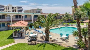 A hotel with a swimming pool, outdoor seating, and palm trees.