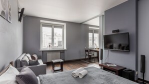 A modern hotel room with a large bed, a desk, a chair, a TV, and a window with a city view. - Studio near Central Department Store (Minsk)