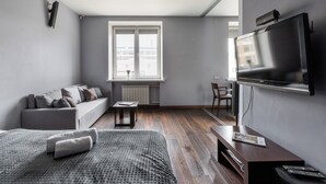 A modern living room with a sofa, a bed, a TV, and a window with a view of buildings. - Studio near Central Department Store (Minsk)