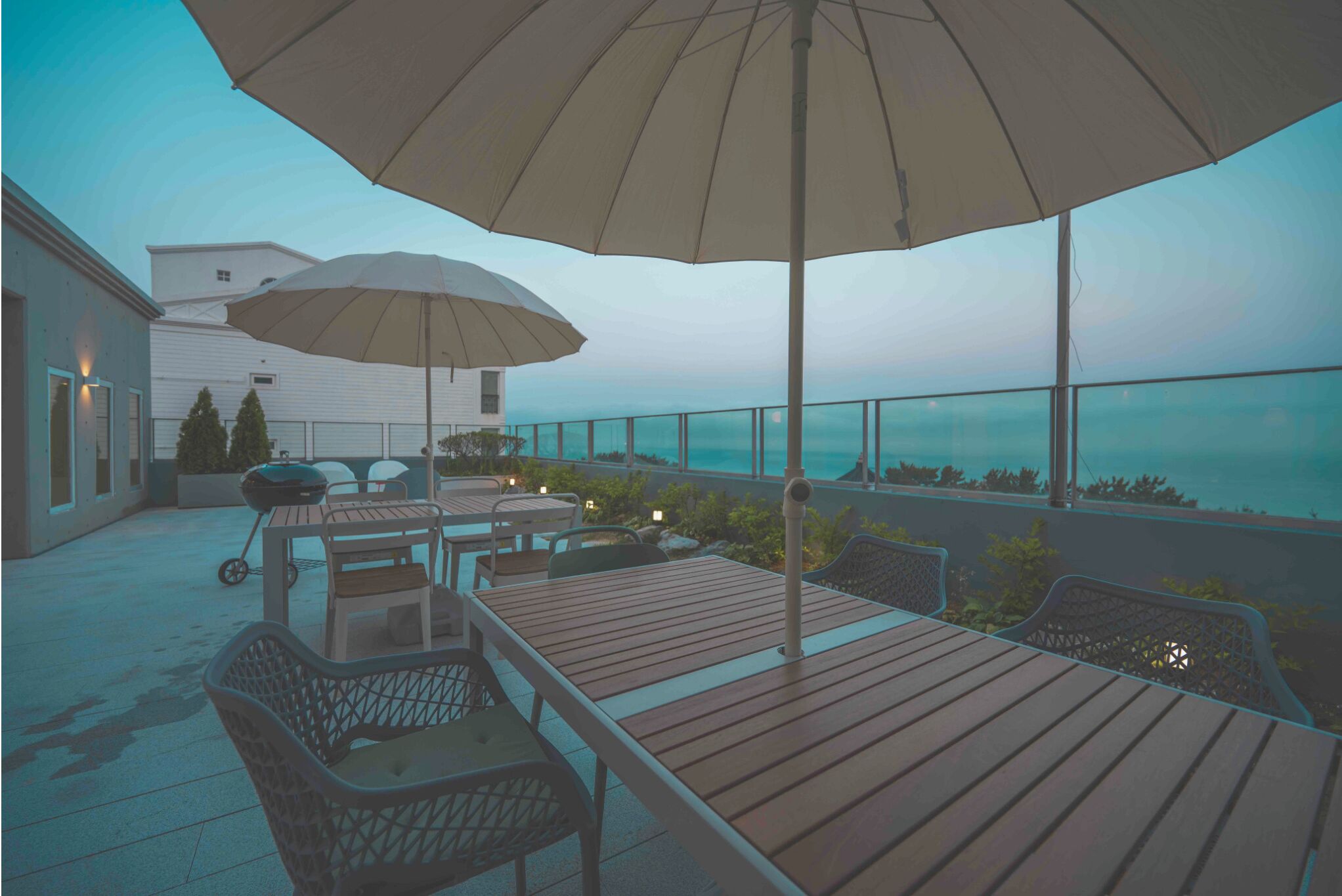 Eine Terrasse im Freien mit Holztischen und -stühlen, einem großen Sonnenschirm und Blick auf das Meer.