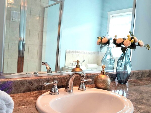 A bathroom with a marble countertop, a sink with two faucets, a large mirror, and a vase with flowers.