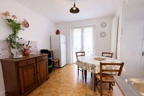 Uma cozinha com uma mesa de jantar, cadeiras, uma geladeira e um relógio na parede.