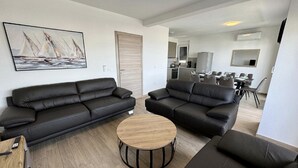 A modern living room with two black leather sofas, a wooden coffee table, and a painting of sailboats on the wall.