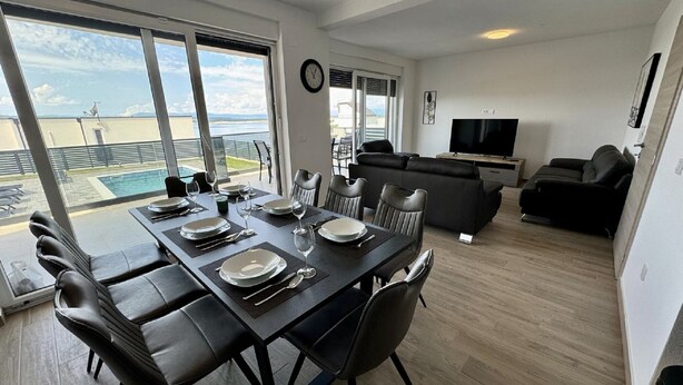 A modern living room with a flat-screen TV, a sofa, and a dining area with a table set for four.