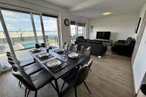 Una sala de estar moderna con un televisor de pantalla plana, un sofá y un comedor con una mesa lista para cuatro personas.