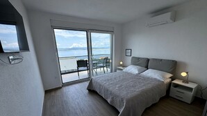 A bedroom with a bed, bedside tables, a chair, and a view of the sea through a sliding door.