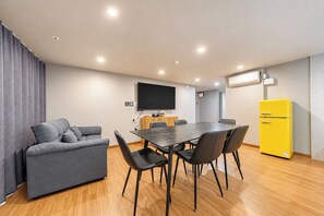 Ein modernes Wohnzimmer mit einer Couch, einem Esstisch mit Stühlen, einem Flachbildfernseher und einem gelben Kühlschrank.