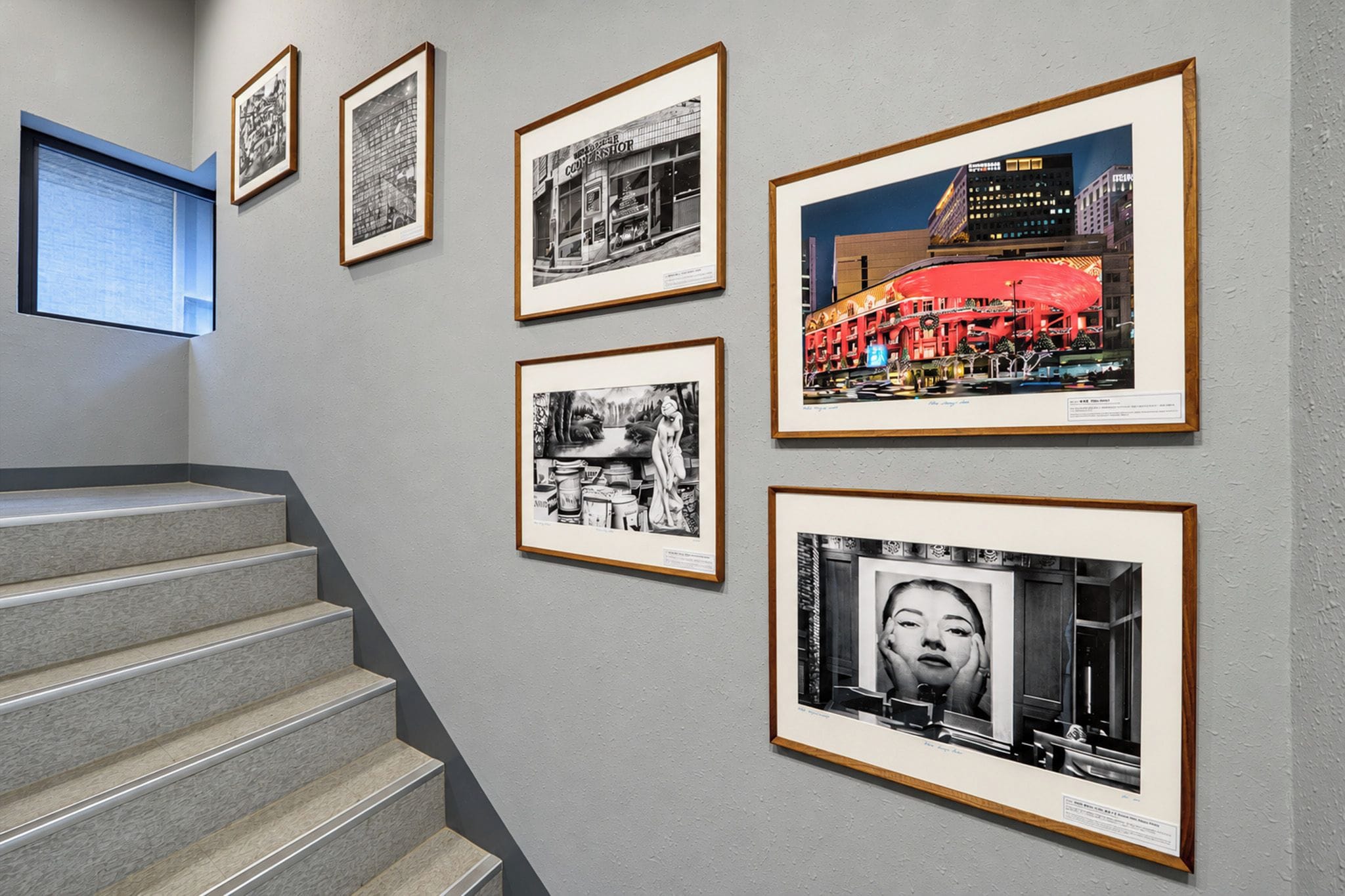 Una escalera con barandilla y peldaños, que conduce a una pared con fotografías blanco y negro enmarcadas.