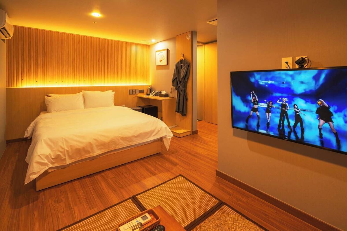 Une chambre d’hôtel dotée d’un grand lit, d’un téléviseur à écran plat, d’un plancher en bois et d’une étagère fixée au mur.
