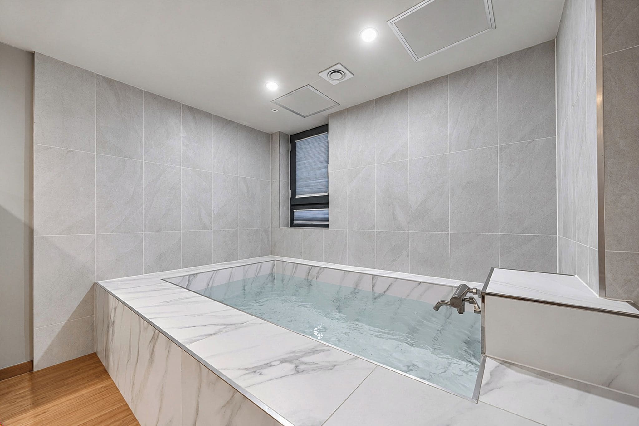 Un baño moderno con una bañera de mármol, una ventana e iluminación empotrada en el techo.