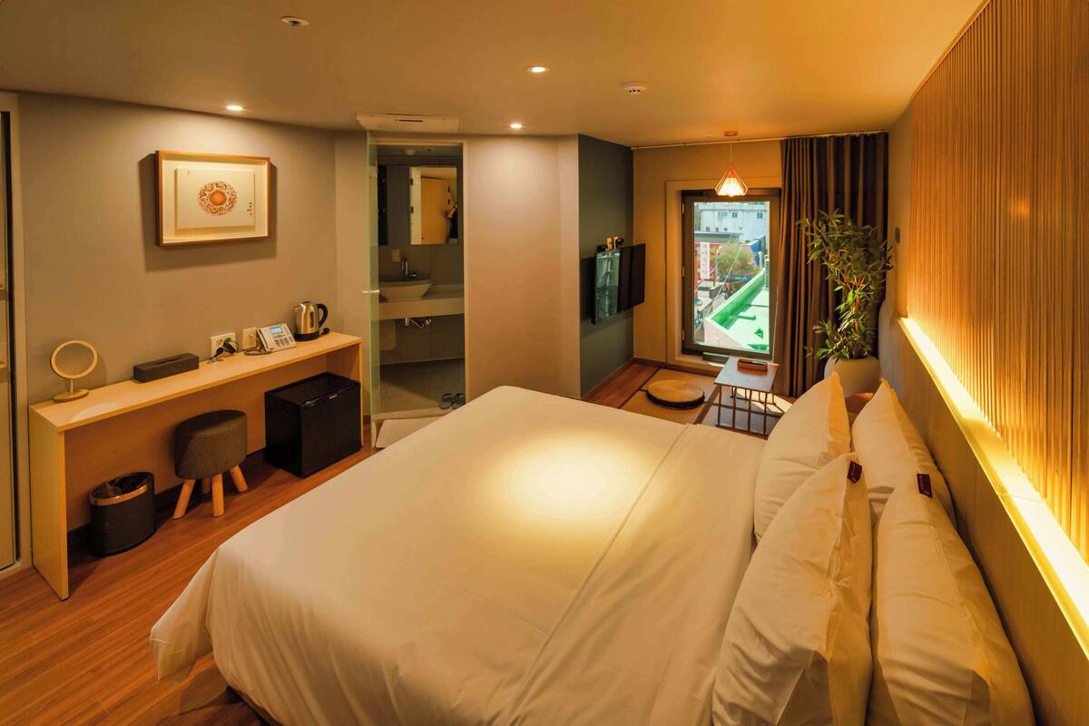 Une chambre d’hôtel moderne, dotée d’un grand lit, d’un bureau avec un ordinateur, d’un miroir et offrant une vue sur l’extérieur.