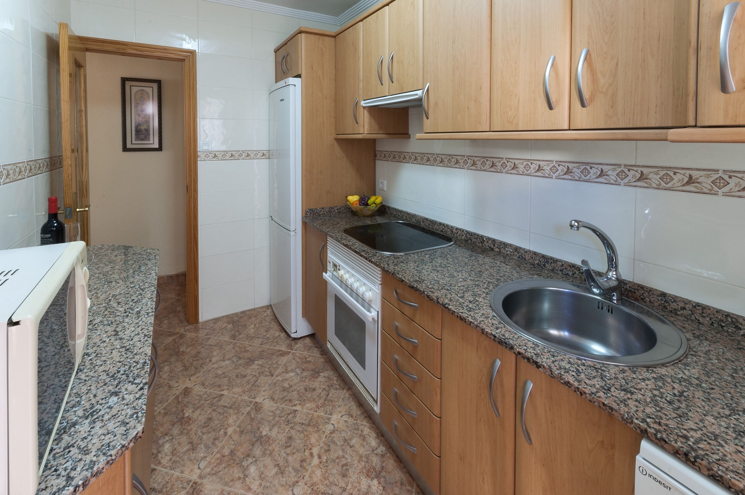 Una cocina con encimeras de granito, armarios de madera, pileta de acero inoxidable, horno empotrado y refrigerador.