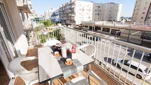 Ein Balkon mit Tisch und Stühlen, der auf eine Straße mit parkenden Autos und Gebäuden blickt.