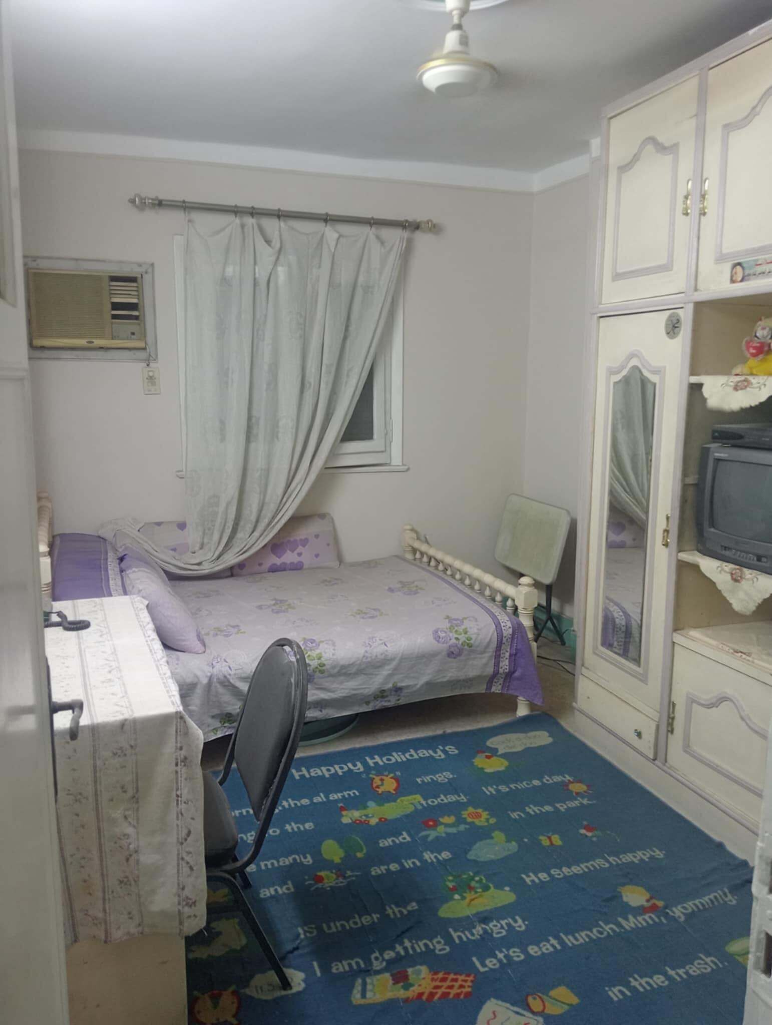 A small bedroom with a single bed, a desk, a chair, a wardrobe, and a television.