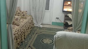 A room with a bed, a television, a ceiling fan, and a patterned rug. - Beautiful Apartment with 2 Bdr and 2 Living Rooms (Ard El lewa, El Mohandessin)