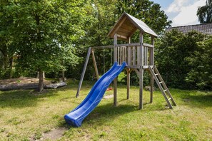 Explore the fun of a park play structure with a slide and climbing ladder amidst lush greenery.