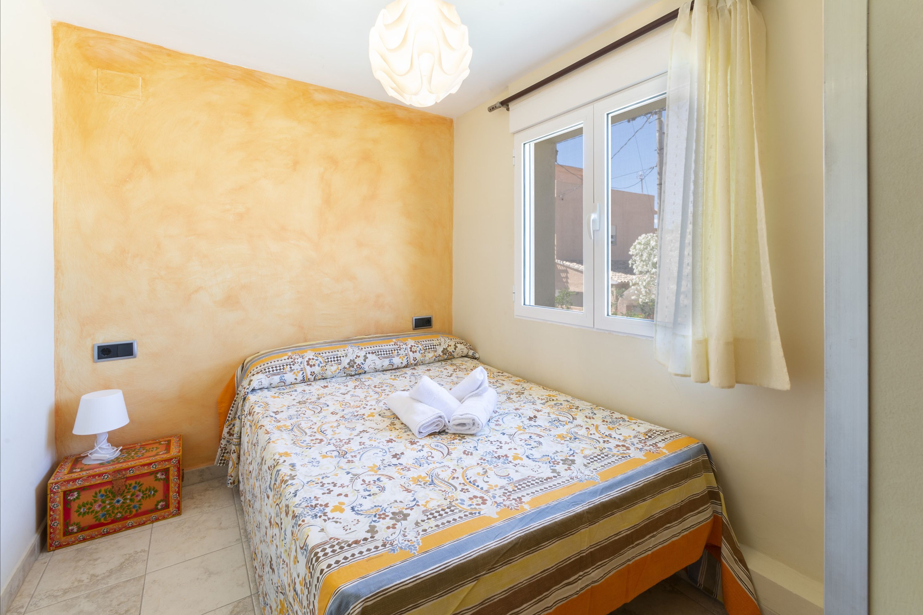 A bedroom with a bed, a nightstand, a lamp, and a window with curtains.