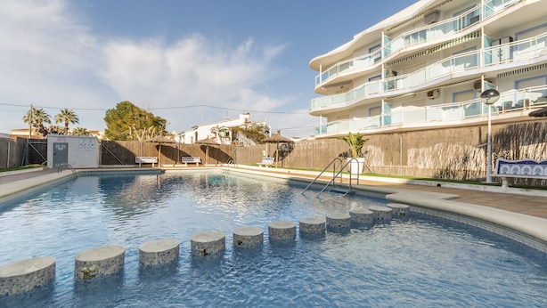 A swimming pool with circular steps leading into it, surrounded by a building with balconies and a clear sky. - Apartment Egeu in D nia (Denia)