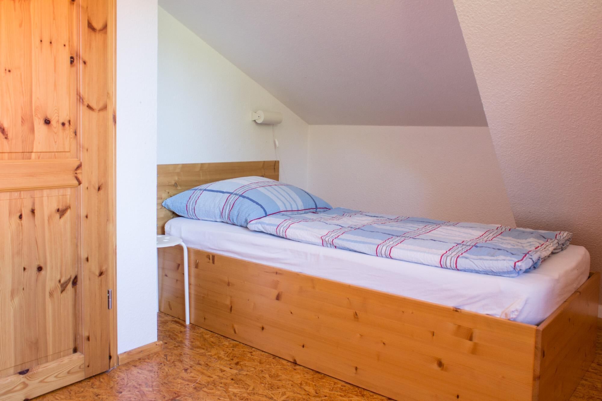 A single wooden bed with a headboard, a white wall, and a wooden door.
