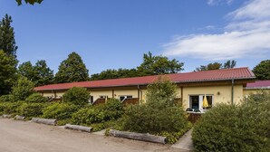 Un bâtiment à deux étages, surmonté d’un toit recouvert de tuiles rouges, entouré d’une végétation luxuriante et d’arbres.