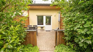Un espace patio avec une table et des chaises, une clôture en bois et une porte donnant accès à un bâtiment.