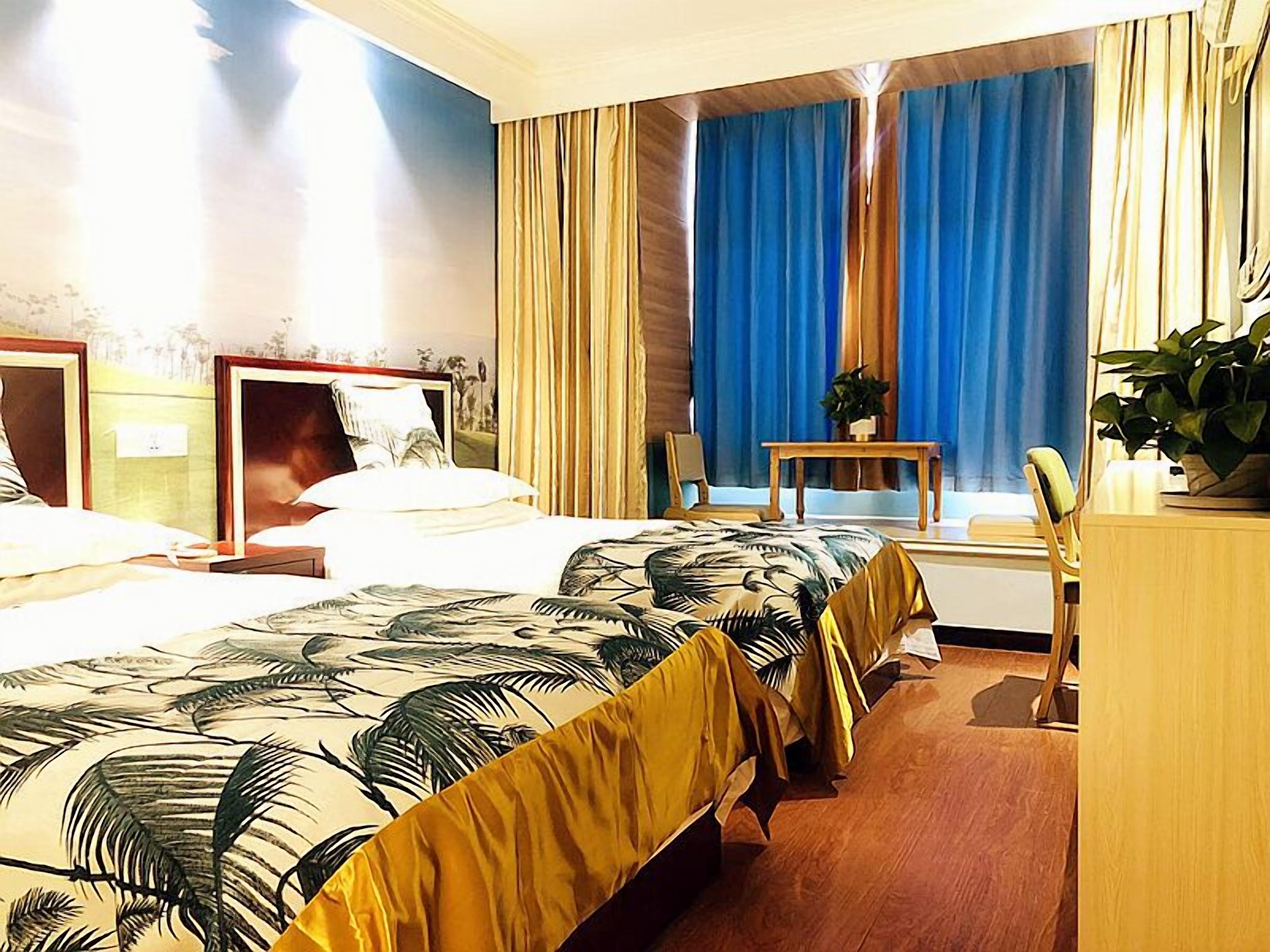 Une chambre d’hôtel avec deux lits, un bureau, une chaise, une plante et une fenêtre avec des rideaux.