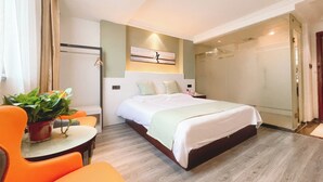 A modern hotel room with a large bed, a seating area with orange chairs, a small table, and a potted plant. - East Maples Inn Wanda (Wuxi)