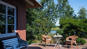 A patio with a bench, two wicker chairs, and a small table. - Right on the water: large thatched-roof house for 8 people, fireplace and garden (Breiholz)
