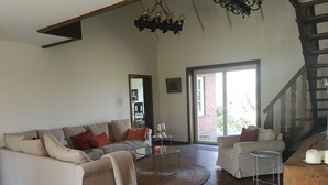 A spacious living room with a large sofa, a smaller armchair, a coffee table, and a staircase. - Right on the water: large thatched-roof house for 8 people, fireplace and garden (Breiholz)