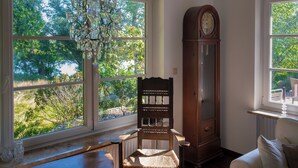A room with large windows, a wooden chair, a tall wooden clock, and a chandelier. - Right on the water: large thatched-roof house for 8 people, fireplace and garden (Breiholz)