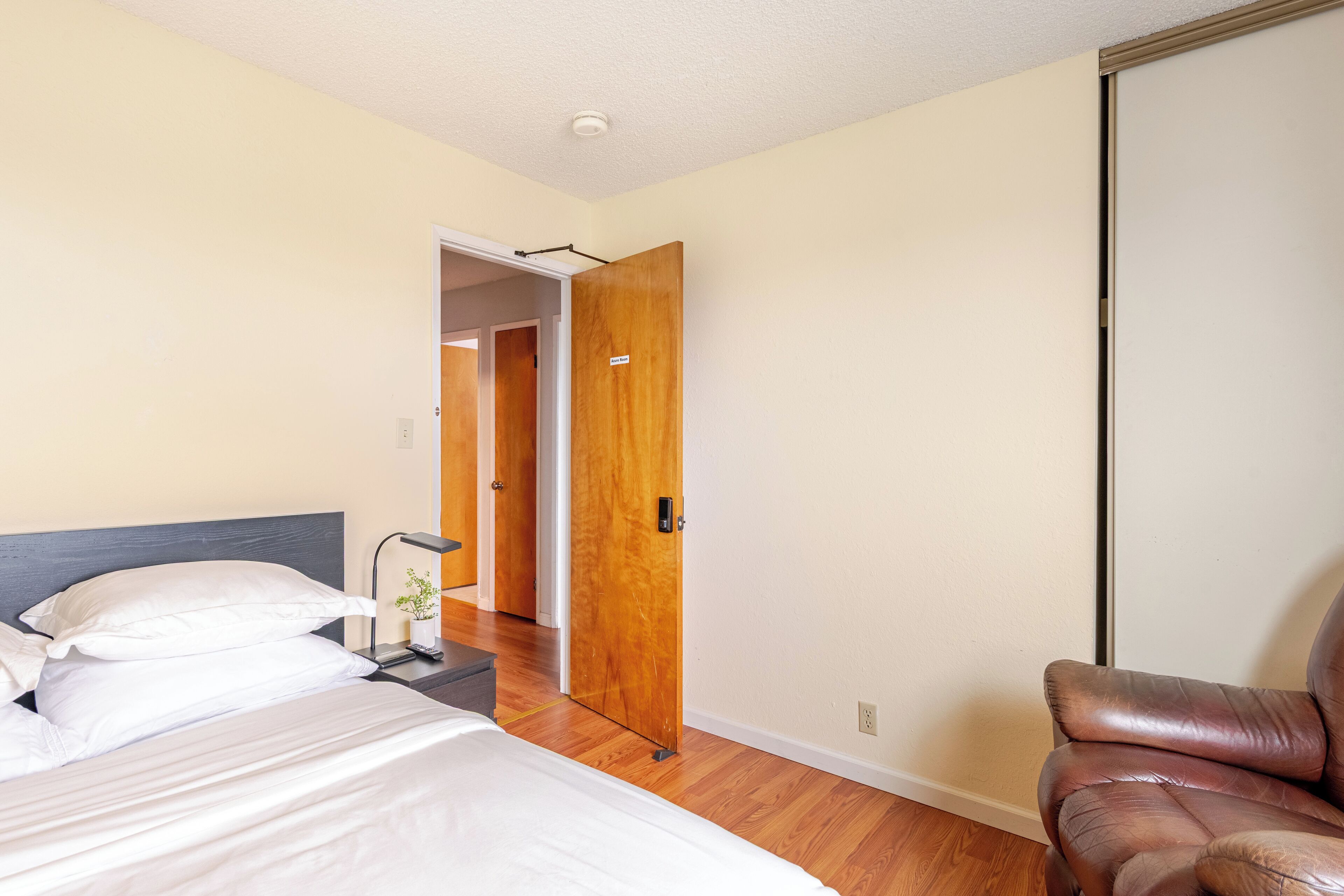 Quarto de hotel com uma cama, uma cadeira e uma porta de madeira que dá para outro espaço.