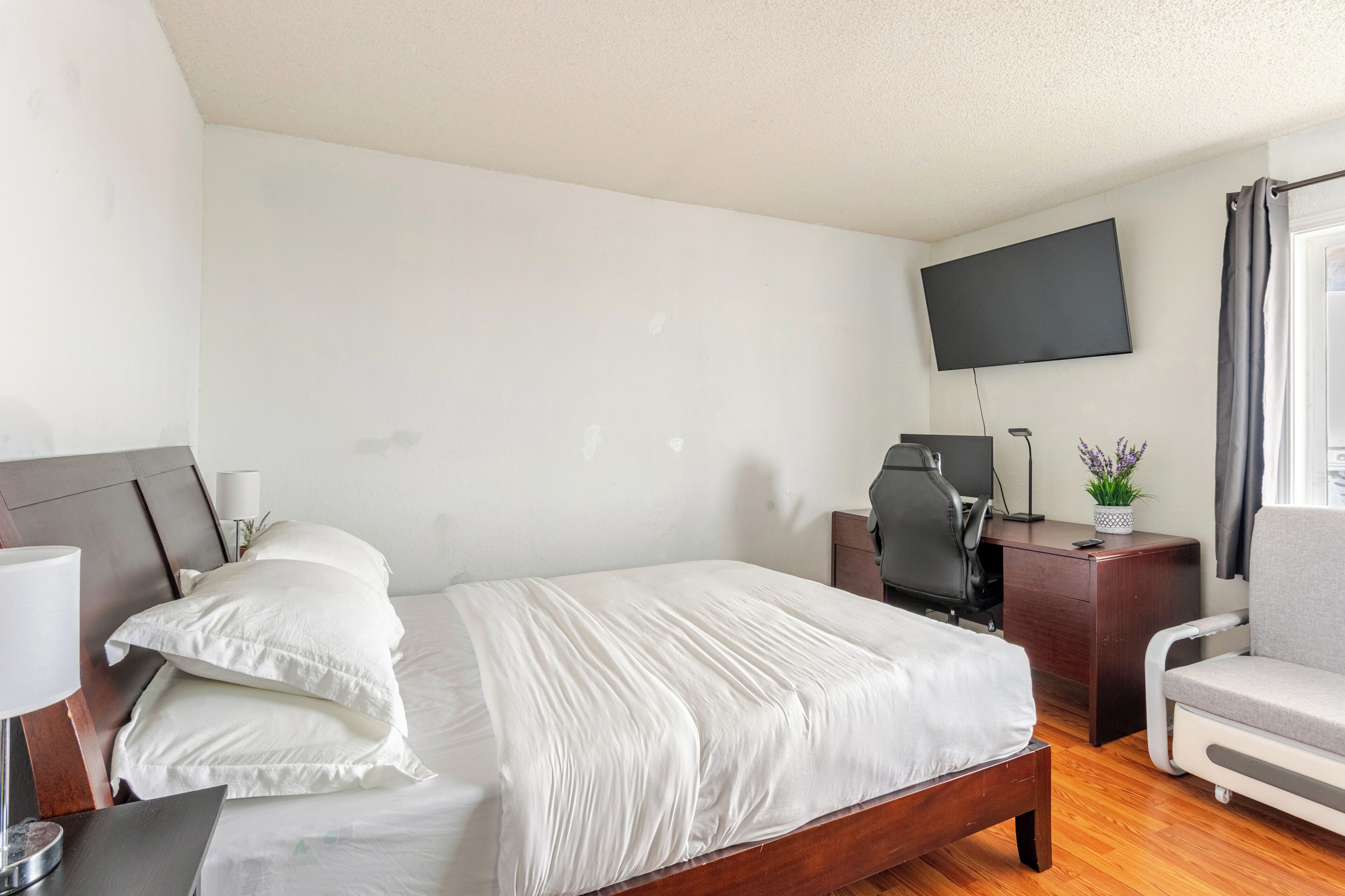 A hotel room with a bed, a desk, a chair, a TV, and a window with curtains.