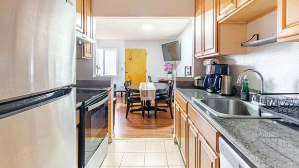 Una cocina con armarios de madera, un refrigerador de acero inoxidable, encimera de granito y un comedor con mesa y sillas.