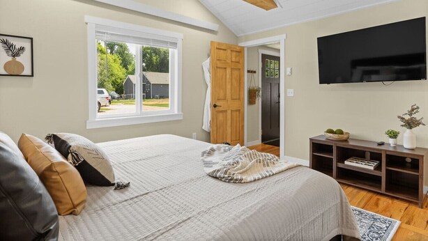 A bedroom with a bed, a window, a door, a TV, and a console table. - Crow peak Cabin: Peaceful stay (Spearfish)