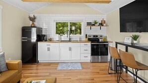 A modern kitchen with white cabinets, a black refrigerator, a stainless steel oven, and a wooden ceiling. - Crow peak Cabin: Peaceful stay (Spearfish)