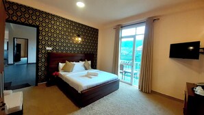 Habitación de hotel con una cama grande, televisión, balcón con vistas y papel tapiz estampado.