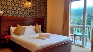 Habitación de hotel con una cama grande, cabecera de madera, mesita de noche con lámpara y vistas al exterior a través de un ventanal.
