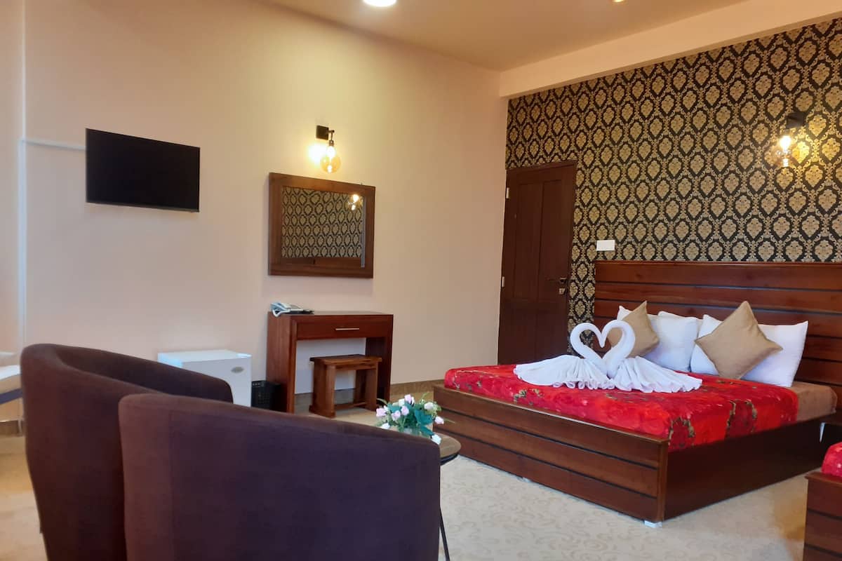 A hotel room with a bed, a desk, a chair, and a TV mounted on the wall.