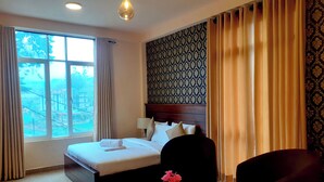 Un cuarto de hotel con una cama grande, una mesita de noche con un florero y una silla, y vista al exterior a través de una ventana.