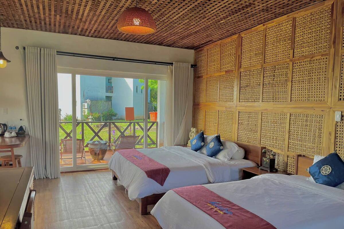 A hotel room with two beds, a wooden ceiling, a balcony with a view, and a table with chairs.