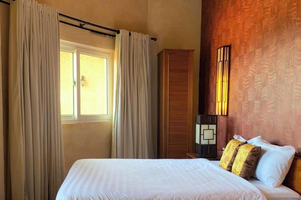 A hotel room with a large bed, curtains, a wardrobe, and a wall-mounted light fixture.