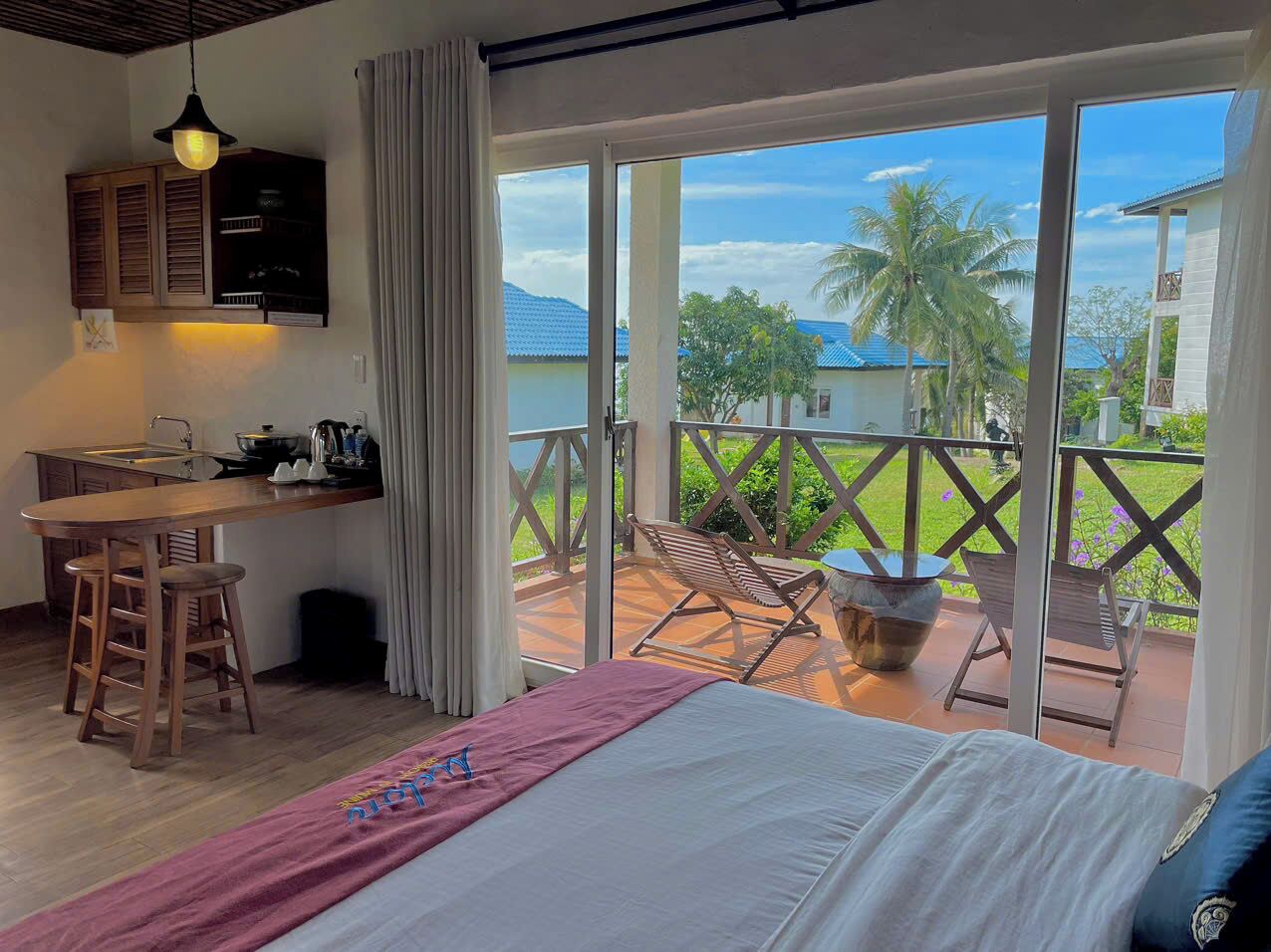 Een kamer met een bed, een bureau en een balkon met stoelen en een tafel.