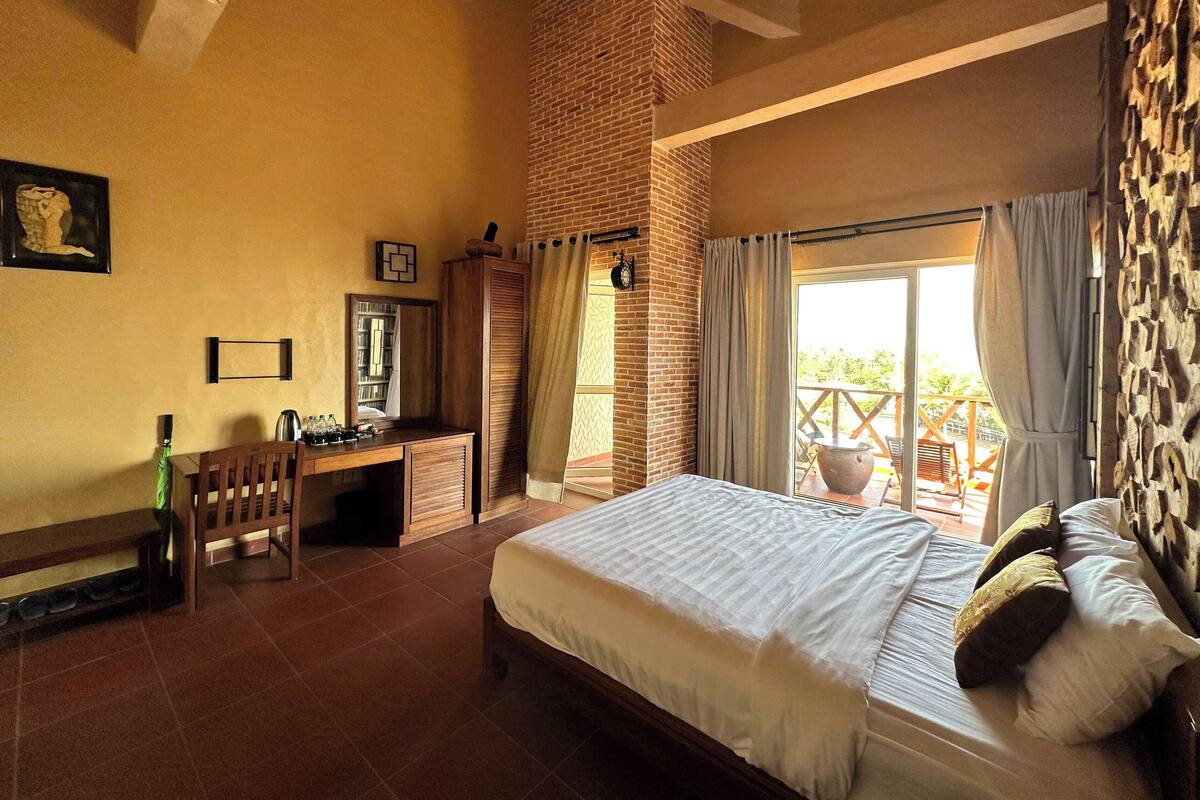 A bedroom with a large bed, a desk, a chair, and a window with curtains.