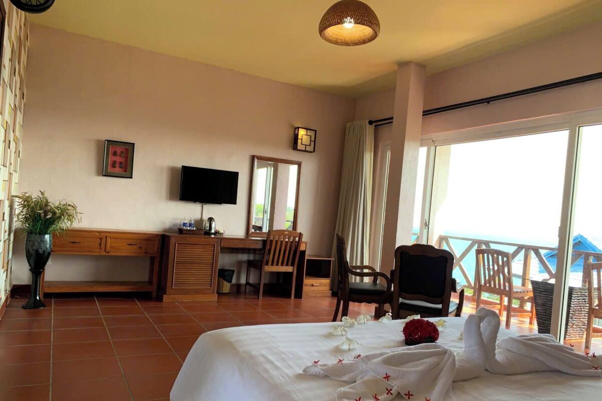 A hotel room with a bed, a desk, a chair, a TV, and a balcony with a view.